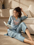 Woman wearing a blue linen co-ord set with floral embroidery and tassel details, sitting and reading a book.