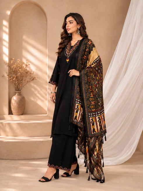 Woman wearing a black embroidered kurti and palazzo set with a colorful printed dupatta, seated on a chair.