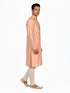 Man wearing a peach silk Kurta Pajama with intricate embroidery on the neckline and cream churidar pants.