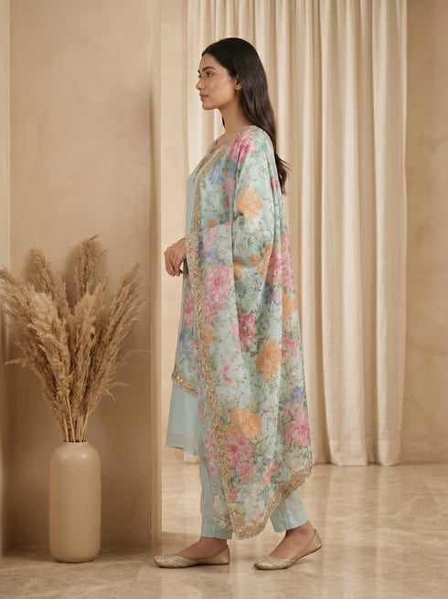 Woman wearing a sky blue kurta set with floral dupatta, featuring intricate neckline embroidery and a shimmering border.
