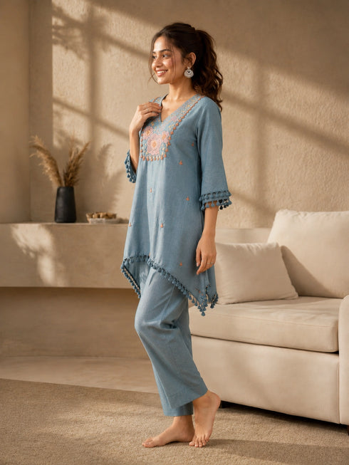 Woman wearing a blue linen co-ord set with floral embroidery and tassel details, sitting and reading a book.
