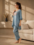 Woman wearing a blue linen co-ord set with floral embroidery and tassel details, sitting and reading a book.