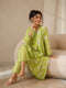 Woman wearing a lime green printed kurti and chevron patterned pants, sitting on a cream sofa.