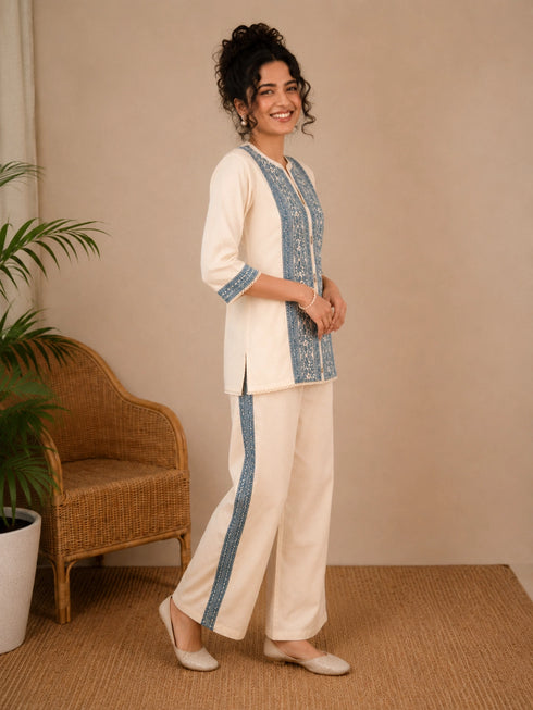 Woman wearing a cream kurta with blue paisley print, showcasing intricate embroidery and a band collar neckline.