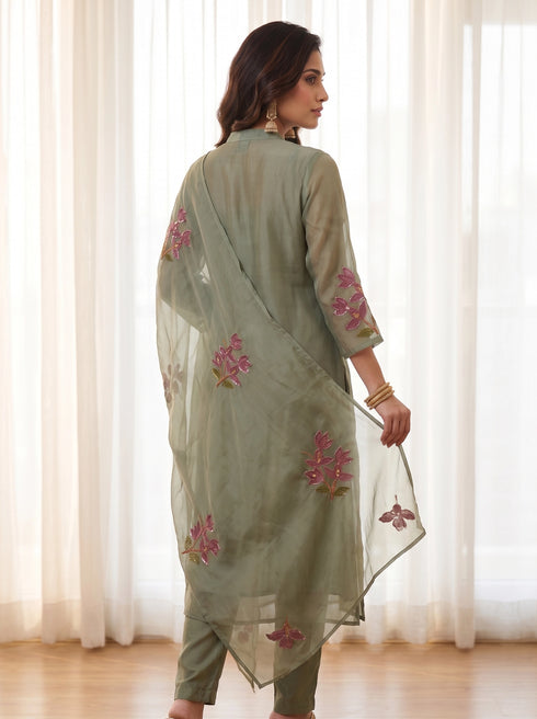 Woman wearing a green floral embroidered kurta set with a sheer dupatta and gold heels.