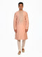 Man wearing a peach silk Kurta Pajama with intricate embroidery on the neckline and cream churidar pants.