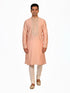Man wearing a peach silk Kurta Pajama with intricate embroidery on the neckline and cream churidar pants.