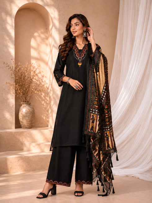 Woman wearing a black embroidered kurti and palazzo set with a colorful printed dupatta, seated on a chair.