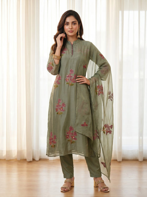 Woman wearing a green floral embroidered kurta set with a sheer dupatta and gold heels.