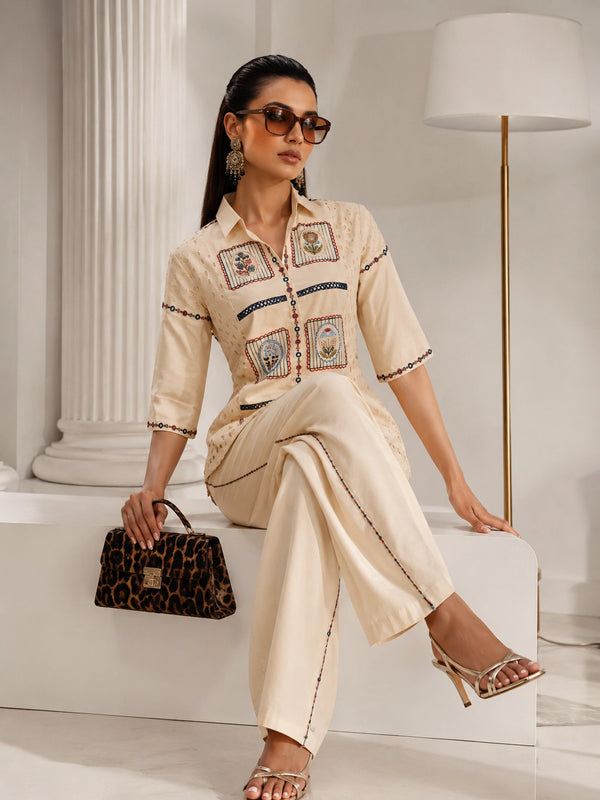 Woman wearing a cream embroidered shirt and wide-leg pants, sitting with a leopard print handbag.