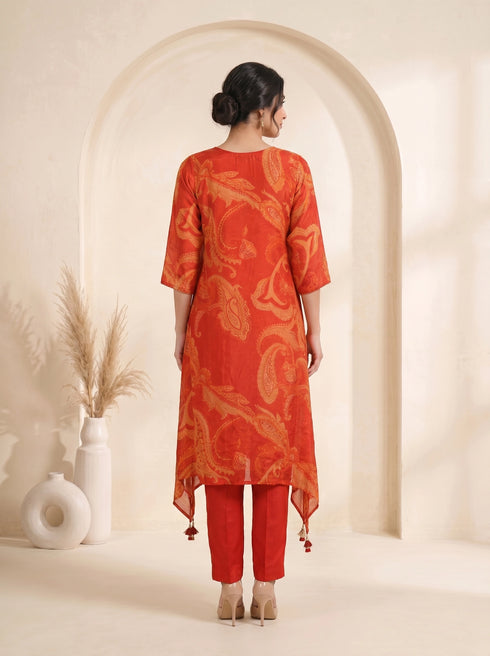 Woman wearing a vibrant orange kurti with paisley print and matching pants, adorned with neckline embellishments.