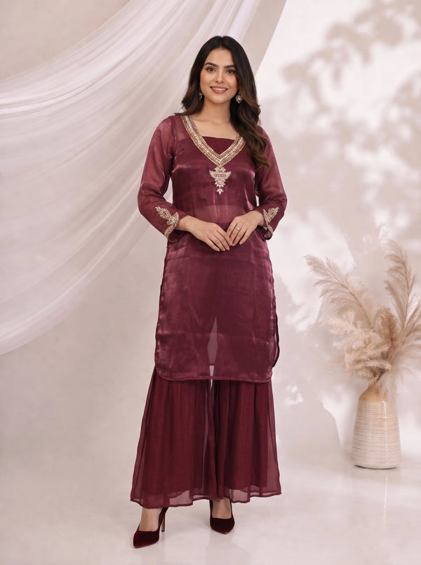 Woman wearing a maroon embroidered kurta with flowing sharara pants, featuring gold neckline and cuff details.