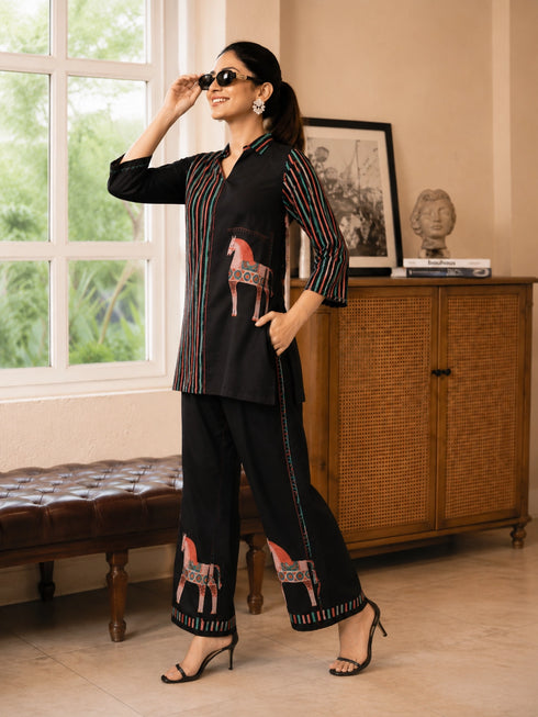 Woman wearing a cream and black striped pajama set with horse prints, sitting on a bench.