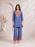 Woman wearing a blue embroidered kurta and matching wide-leg pants with a geometric border, styled with nude heels.