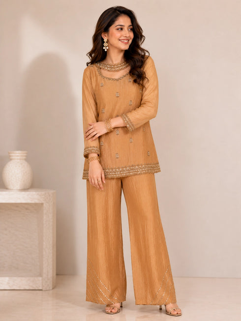 Woman wearing a mustard embroidered Sharara with intricate embellishments on the neckline and hem.