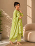 Woman wearing a lime green printed kurti and chevron patterned pants, sitting on a cream sofa.