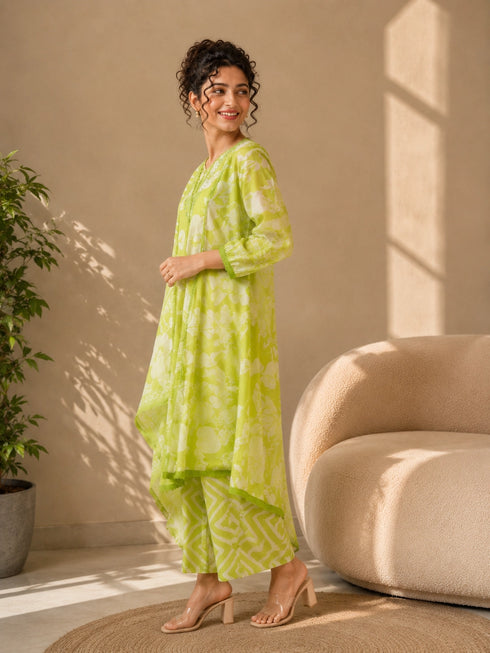 Woman wearing a lime green printed kurti and chevron patterned pants, sitting on a cream sofa.
