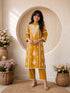 Woman wearing a mustard yellow embroidered kurta and pants set, sitting indoors with flowers.