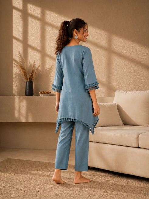 Woman wearing a blue linen co-ord set with floral embroidery and tassel details, sitting and reading a book.