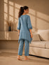Woman wearing a blue linen co-ord set with floral embroidery and tassel details, sitting and reading a book.