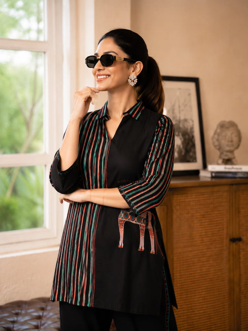 Woman wearing a cream and black striped pajama set with horse prints, sitting on a bench.