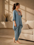 Woman wearing a blue linen co-ord set with floral embroidery and tassel details, sitting and reading a book.