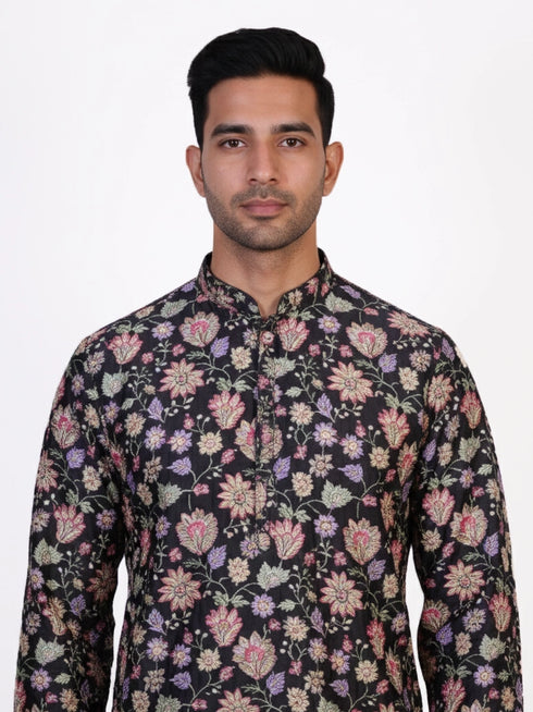 Man wearing a dark multi-color floral print kurta and white churidar pants, traditional ethnic wear.