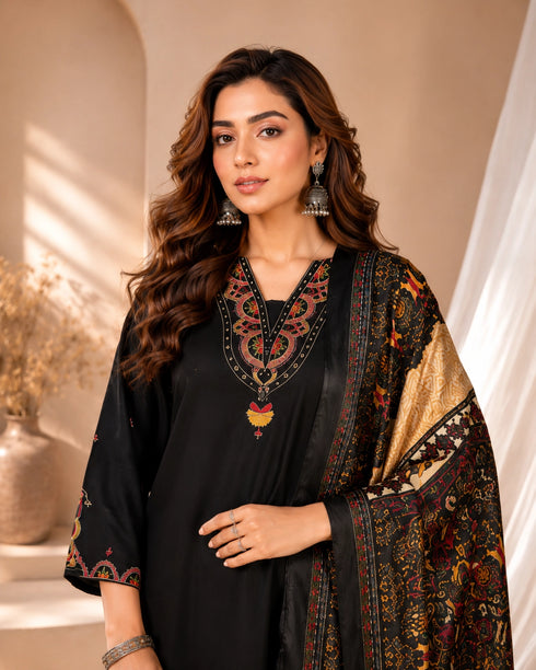 Woman wearing a black embroidered kurti and palazzo set with a colorful printed dupatta, seated on a chair.