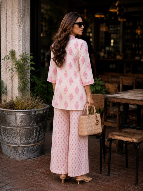 Woman wearing a pink floral print cotton kurta and matching pants, sitting at a table.