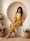 Woman wearing a mustard yellow embroidered kurta and pants set, sitting indoors with flowers.