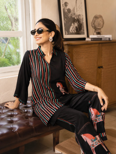 Woman wearing a cream and black striped pajama set with horse prints, sitting on a bench.