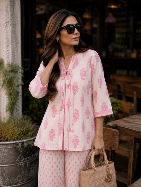 Woman wearing a pink floral print cotton kurta and matching pants, sitting at a table.