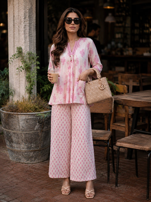 Woman wearing a pink floral print cotton kurta and matching pants, sitting at a table.