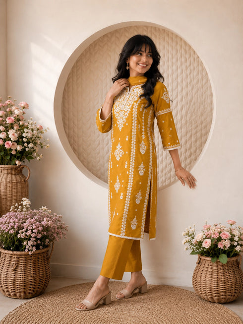 Woman wearing a mustard yellow embroidered kurta and pants set, sitting indoors with flowers.