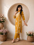 Woman wearing a mustard yellow embroidered kurta and pants set, sitting indoors with flowers.