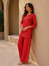 Woman wearing a vibrant red embroidered kurta and pants set with gold accents, sitting casually.