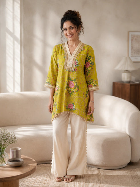 Woman wearing a yellow floral print kurta with cream pom-pom pants, sitting on a sofa and reading a book.