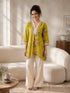 Woman wearing a yellow floral print kurta with cream pom-pom pants, sitting on a sofa and reading a book.