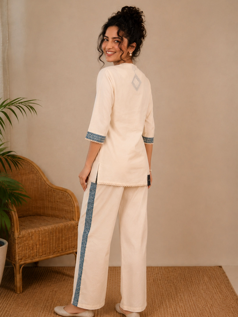 Woman wearing a cream kurta with blue paisley print, showcasing intricate embroidery and a band collar neckline.