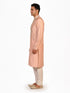 Man wearing a peach silk Kurta Pajama with intricate embroidery on the neckline and cream churidar pants.