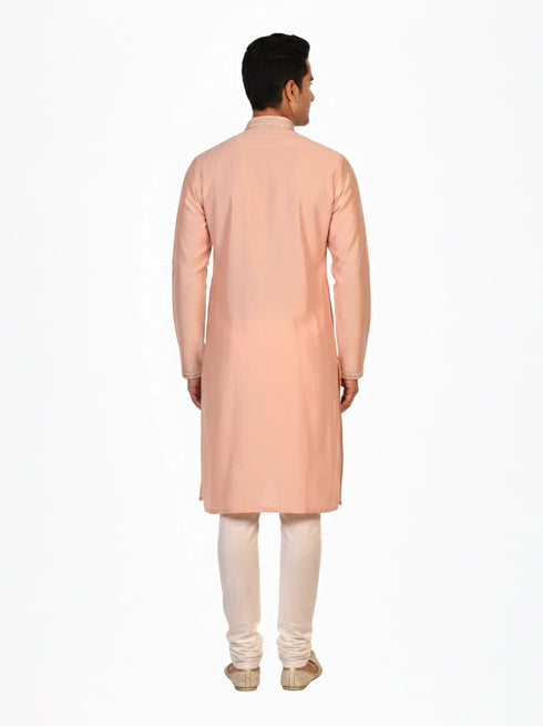 Man wearing a peach silk Kurta Pajama with intricate embroidery on the neckline and cream churidar pants.