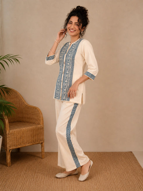 Woman wearing a cream kurta with blue paisley print, showcasing intricate embroidery and a band collar neckline.