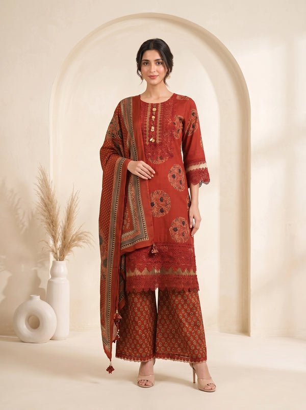 Woman wearing a rust orange printed kurti set with palazzo pants and a dupatta, showcasing intricate patterns and lace details.