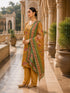 Woman wearing a mustard floral print kurta set with green dupatta and gold embellished flats.