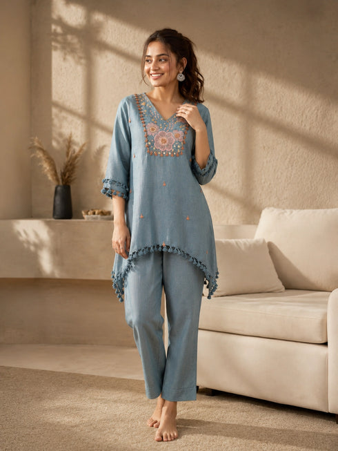 Woman wearing a blue linen co-ord set with floral embroidery and tassel details, sitting and reading a book.
