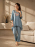 Woman wearing a blue linen co-ord set with floral embroidery and tassel details, sitting and reading a book.