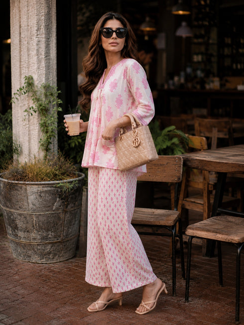 Woman wearing a pink floral print cotton kurta and matching pants, sitting at a table.