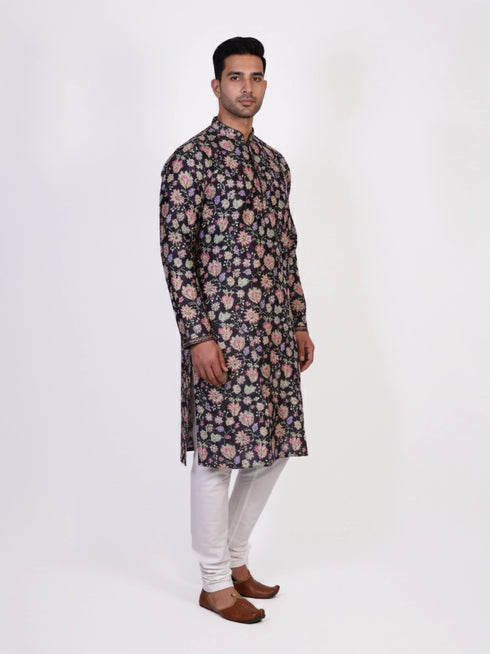 Man wearing a dark multi-color floral print kurta and white churidar pants, traditional ethnic wear.