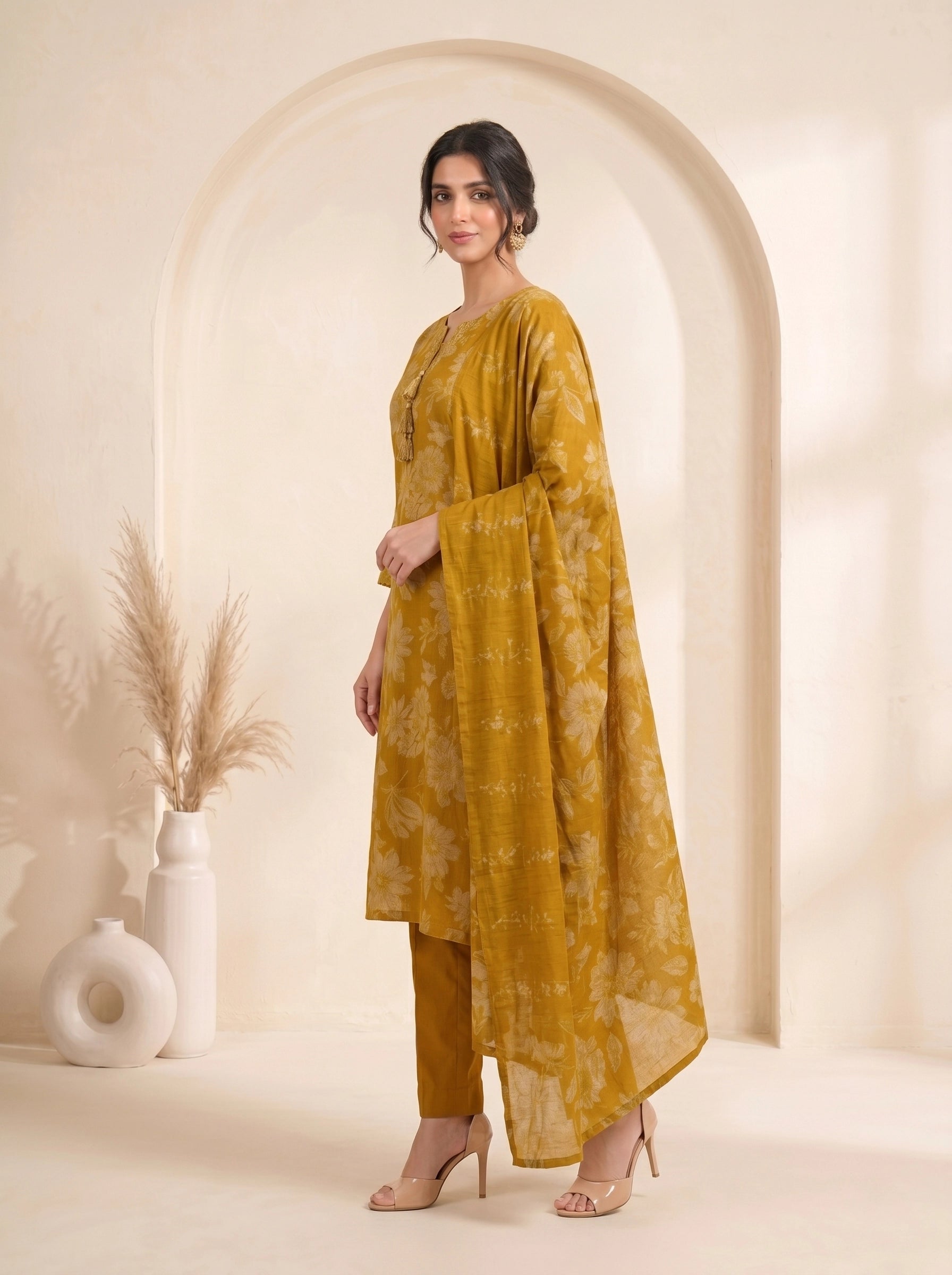 Woman wearing a mustard yellow floral print cotton kurti set with a dupatta and beige heels.