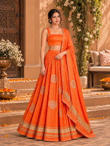 Woman wearing a vibrant rust orange embroidered lehenga choli set with a matching dupatta.